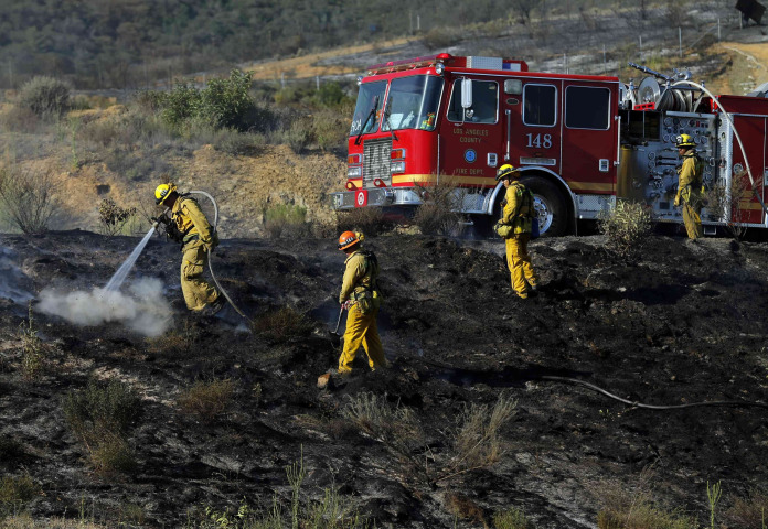 Image: A Los Angeles Country fire crew works on a hillside putting out hotspots on the Coco Fire in San Marcos California