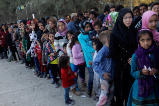 Image: Migrants wait in line to get food in a reception center