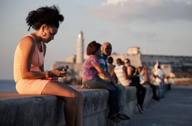 Image: A woman uses her cellphone as she sits on the Malecon in Havana, Cuba