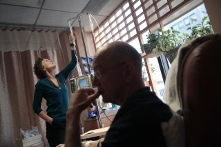 Image: Youssef Cohen, 68, undergoes cancer treatment as his wife Lindsay Wright checks his medication drip