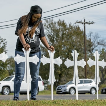 Image: Sheree Rumph of San Antonio prays over two of the 26 crosses erected in memory of the people killed