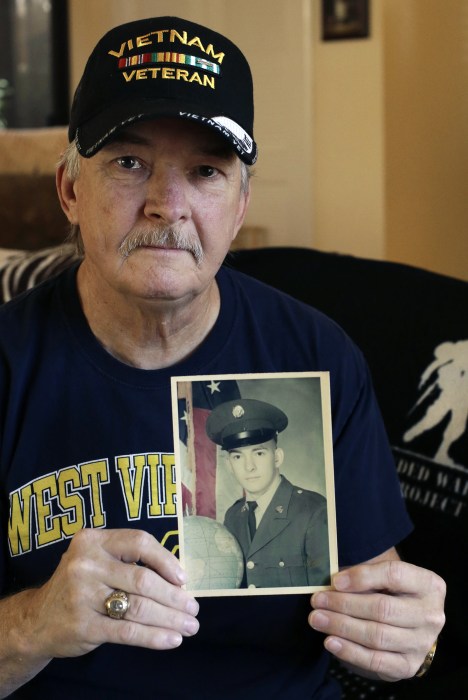   Image: Mike Baughman holds a photo of him from 1971 in his US Army uniform. UU At home 