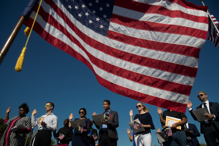 Image: An American flag billows in the wind as immigrants stand and take the oath of allegiance