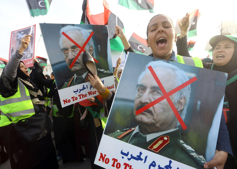 Image: A Libyan woman hits a portrait of Khalifa Haftar with a shoe