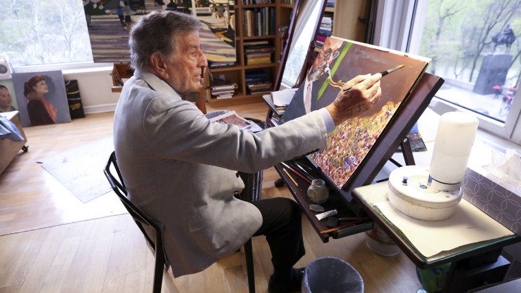 Image: In his New York art studio, Tony Bennett finishes a painting while sitting among several of his completed works.  
